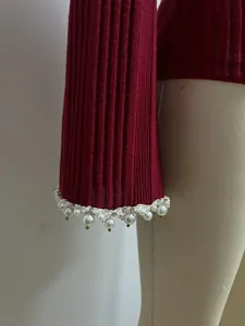 Gros plan détaillé des poignets ornés de perles sur un pull en maille côtelée bordeaux