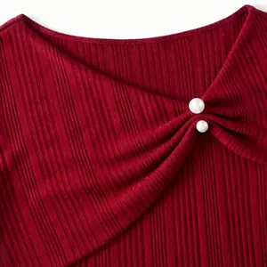 Détail d'un haut en maille côtelée rouge avec encolure asymétrique et perles élégantes.