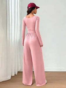 Back view of a slim fit pink long sleeve wide leg jumpsuit in a minimalist setting.