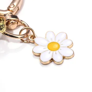 Close-up detail of a white enamel daisy flower charm on a elegant gold-toned keychain
