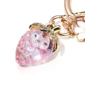 Detailed macro view of a pink translucent strawberry bag charm with golden metal hardware