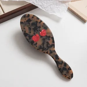 Vue détaillée d'une brosse à cheveux de luxe en acétate avec motif écaille et cerises rouges