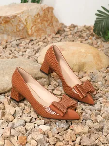 Detail showing the elegant crocodile skin texture and bow on brown chunky heel pumps.