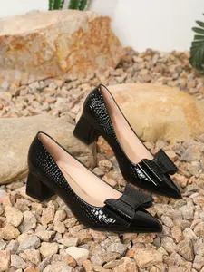 Detailed view of black crocodile-textured block heel pumps with a large bow adornment