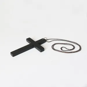 Detailansicht eines minimalistischen schwarzen Kreuzanhängers mit dunkler Metallkugelkette.
