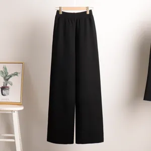Detail view of premium black high-waisted knit wide-leg trousers hanging in a minimalist room.