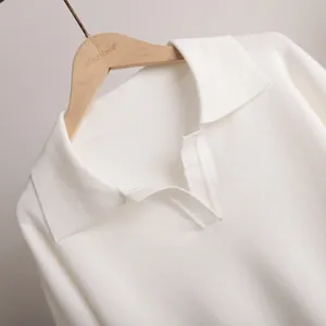Close-up of white knitted polo collar sweater showing detailed fabric texture and V-neckline.