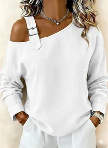 Detalle de blusa blanca de lino con hombros descubiertos y hebilla decorativa en hombro.