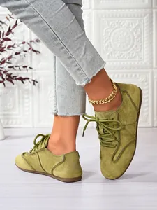 Close-up view of stylish green suede casual lace-up shoes for women with thin brown sole