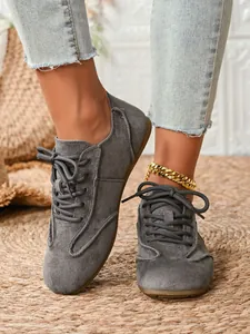 Close-up view of grey suede lace-up casual shoes for women styled with a gold anklet