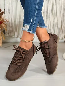 Detailed view of brown suede lace-up shoes paired with blue denim and a gold anklet.