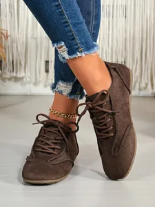 Close-up of brown suede lace-up casual women's shoes styled with blue ripped jeans