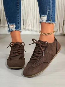 Close-up detail of stylish brown suede lace-up casual sneakers worn with denim jeans.