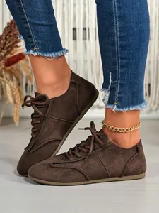 Detail shot of brown suede lace-up casual shoes worn with denim jeans and anklet.