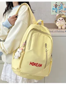 Macro view of stylish yellow backpack worn by model showing red HOKEAM logo detail