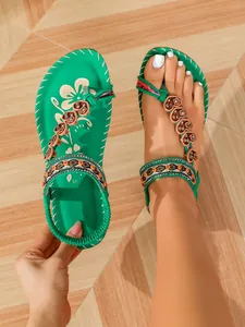 Detailed view of green bohemian flat sandals with heart beads and ethnic patterns on wooden floor