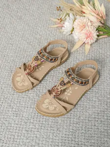 Beige flache Boho-Sandalen mit handgefertigten Perlen und Schmetterlings-Anhängern auf Teppich