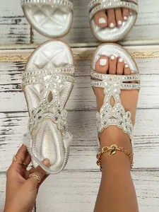 Close-up of silver bohemian flat sandals featuring intricate rhinestone flower patterns.