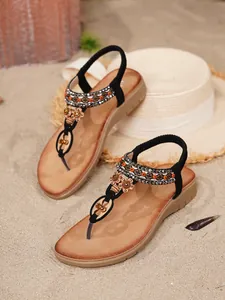 Detailansicht von böhmischen flachen Sandalen mit Strass und Holzperlen auf Strandsand.