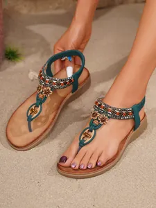 Detailansicht von böhmischen flachen Sandalen mit Perlen und Strass auf Strandsand