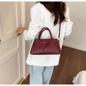 Nahaufnahme einer eleganten bordeauxroten gewebten Tragetasche an einem weißen Blazer