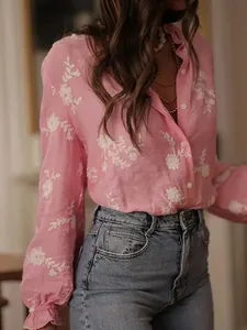 Close-up of elegant pink women's shirt with intricate white floral embroidery details.