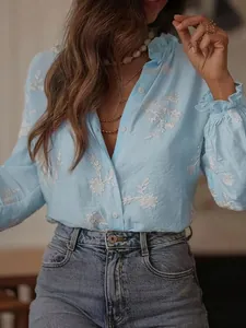 Detail view of light blue floral embroidered blouse with ruffle collar and puff sleeves.