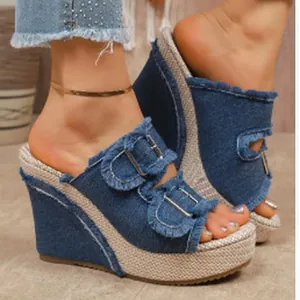 Detail view of denim platform wedge sandals with fringe trim and metal buckles.