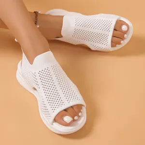 Nahaufnahme von weißen, atmungsaktiven Mesh-Strick-Sandalen an den Füßen vor beigem Hintergrund