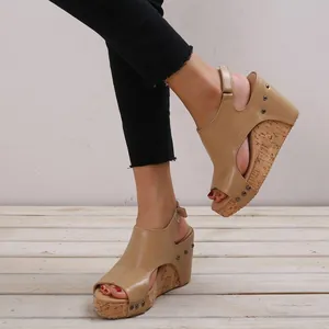 Dettaglio di sandali con zeppa da donna color cuoio con borchie su pavimento in legno