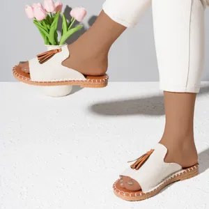 Casual women's flat canvas slides with brown tassel detail shown on feet in a lifestyle setting