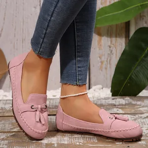 Detailed on-foot view of elegant pink suede tassel loafers with rustic wooden background decor