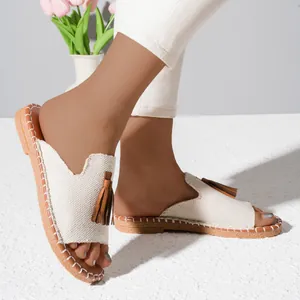 Close-up of beige canvas slippers with brown tassels and stitched flat soles.