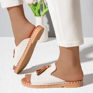 Close-up of beige fabric flat sandals with brown tassels and decorative stitching