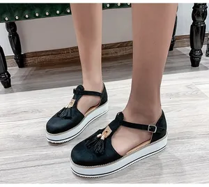 Close-up view of black suede platform sandals with tassel detail worn by a model