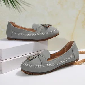 Close-up of grey women's loafers featuring decorative tassels and contrast stitching