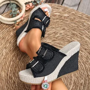 Detailed close-up of black denim wedge slippers with decorative buckles and fringe edges.