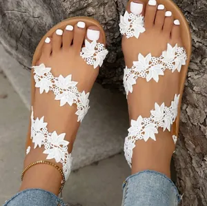 Close-up of bohemian white lace floral straps on flat toe-ring sandals for beach vacations.