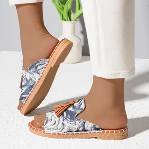 Detailed view of women's flat slide sandals with blue floral print and brown tassels