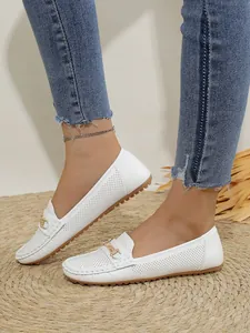 Detailed shot of white perforated loafers for women with gold buckle and soft flat sole.
