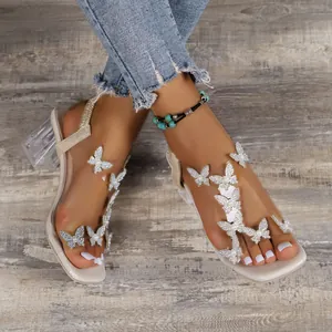 Close-up of white square toe sandals with sparkling butterfly decor and clear block heels.