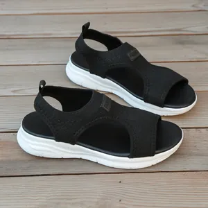 Detailed view of women's black fly-knit platform sandals on a wooden surface.