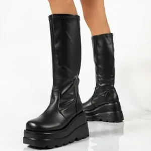 Detail view of woman wearing black faux leather platform tall boots with chunky wedge sole
