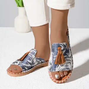 Close-up of women's flat sandals with blue floral pattern and brown tassels.