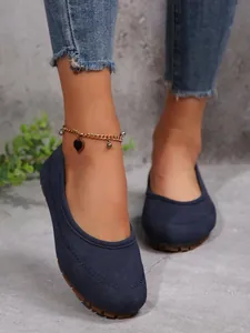 Close-up of navy blue suede flat loafers worn with a gold heart charm anklet and beads