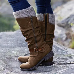 Close-up detail of brown tall knight boots featuring a grey knitted cuff and buckle strap.