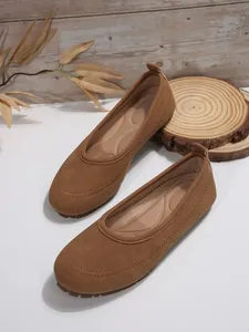 Detail shot of brown suede ballet flats with decorative stitching on white surface.