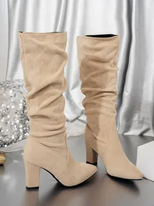 Close-up of beige suede slouchy tall boots with pointed toe and chunky high heel
