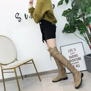 Stylish khaki suede lace-up over-the-knee flat boots worn by a model in a modern studio.