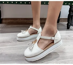 Side view of white platform sandals with T-strap and tassel detail worn by a model